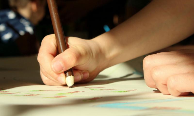 Child drawing a plant on a piece of craft paper.