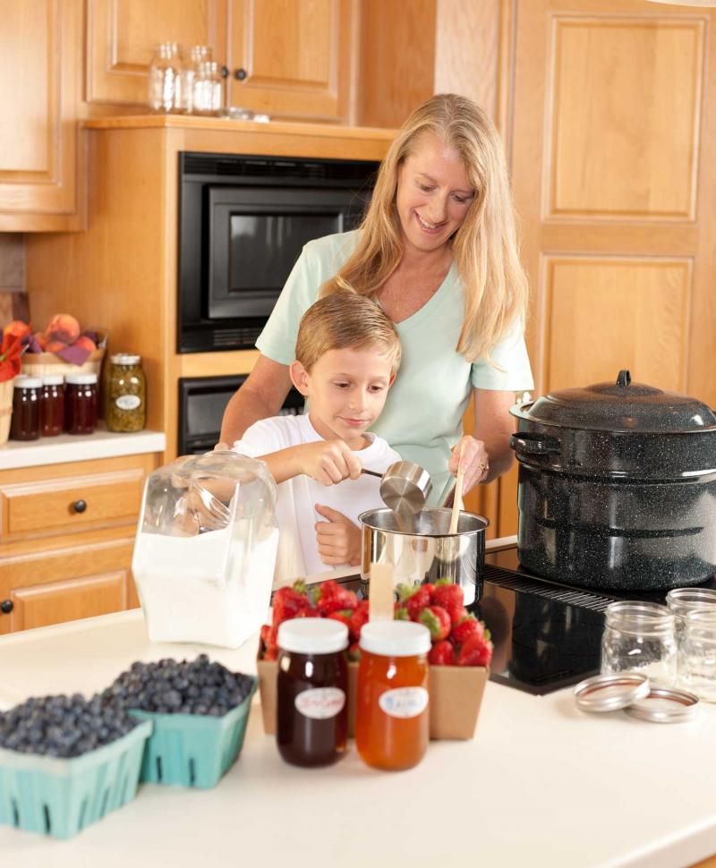 Mother with child cooking homemade jam in a kitchen.