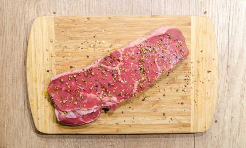 A large piece of seasoned meat on a wooden cutting board.