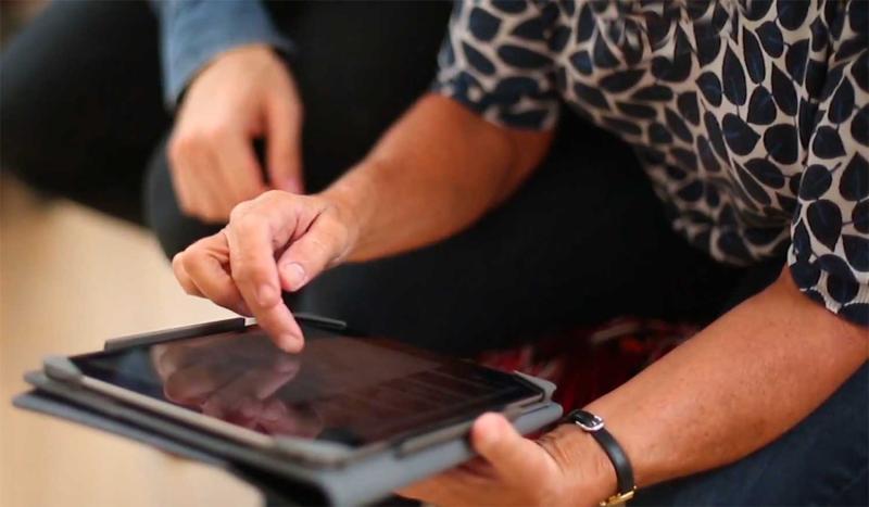 Young adult teaching a tablet lesson to an older adult.