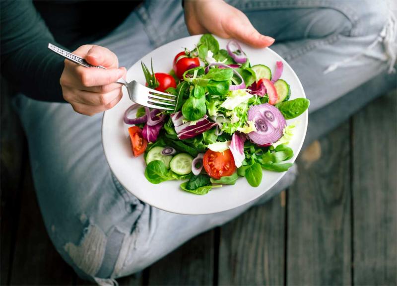 Young woman sitting with a plate of salad in her hands.