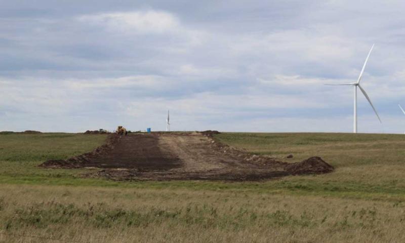 A dirt road leading to a winder energy station in the middle of a grassland area.