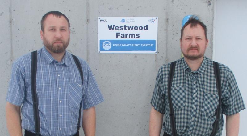 Two men standing in front of a wall with a sign hanging on the wall.