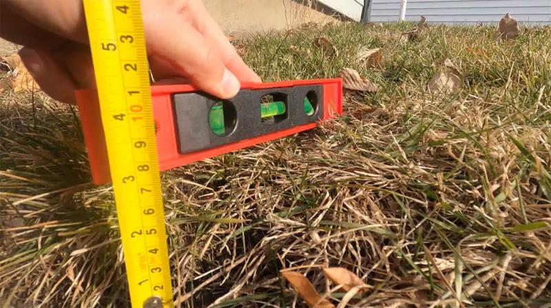 Landowner measuring the slope of an outlet with a measuring tape and level.