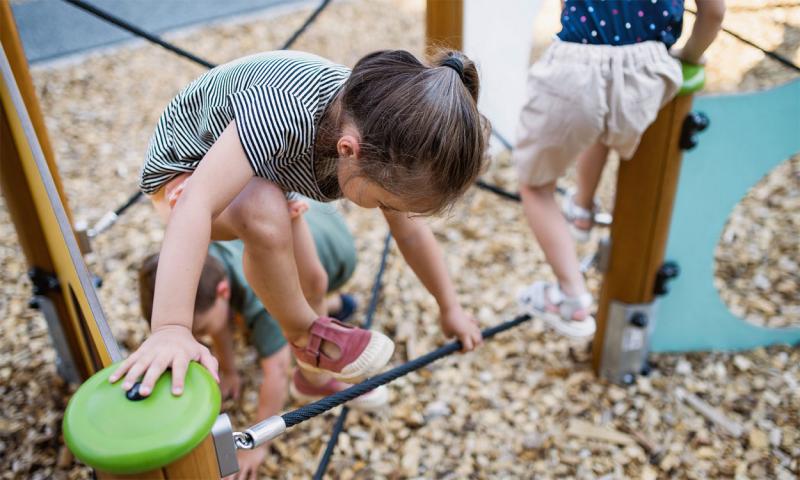 Group of young children climbing on a playground obstacle course.