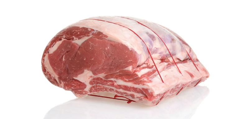 Whole prime rib roast resting on a white countertop.