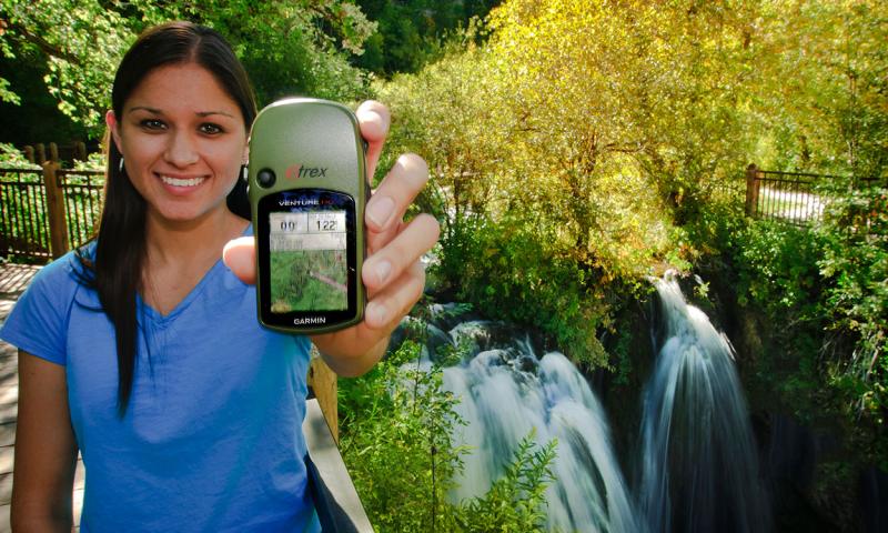 Young woman geocaching with a gps device in a park.