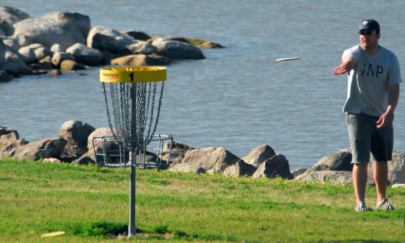 Young man playing disc golf in a park.