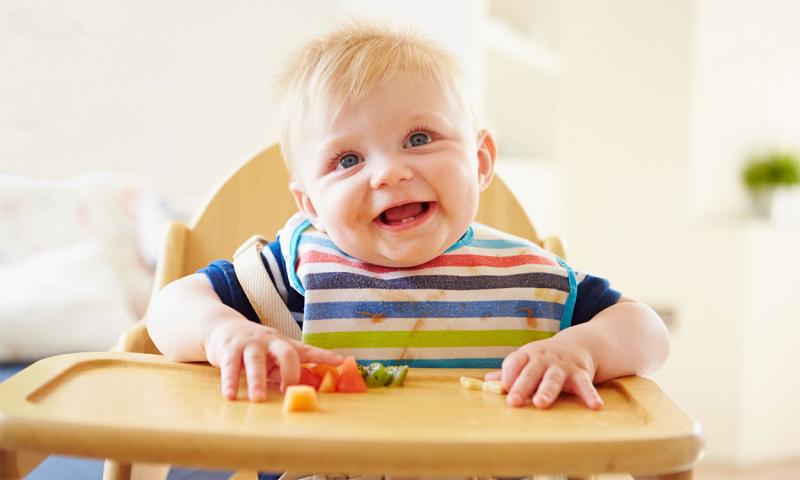 Baby seated at a highchair with a variety of soft, cut-up foods on its tray.