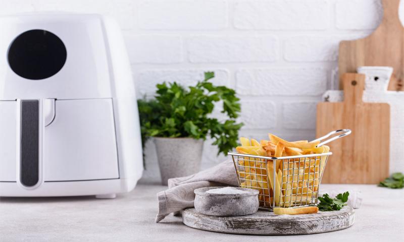White basket-style air fryer on kitchen counter next to a basket of cooked French fries.