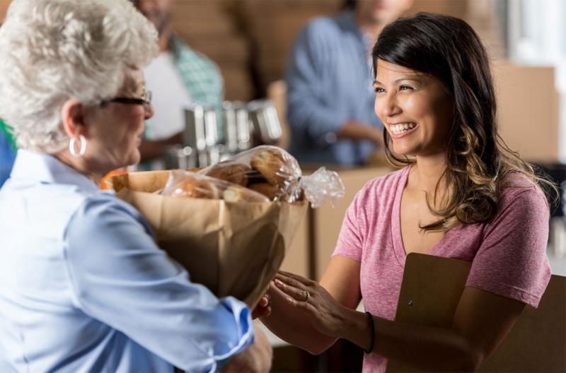 Woman delivering a bag food donations to a food bank manager.