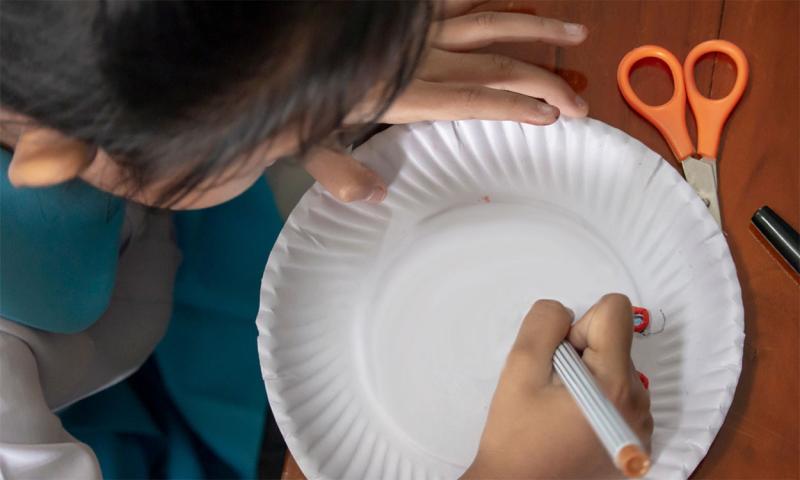 Child drawing on a paper plate with a colored marker.