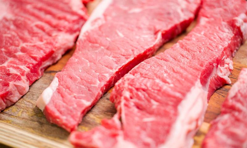 Raw New York strip steaks on a wood cutting board.
