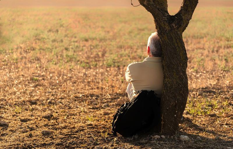 An older man leaning against a tree.