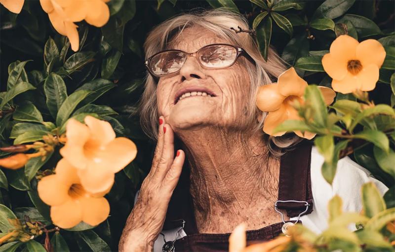An older woman surrounded by beautiful flowers.