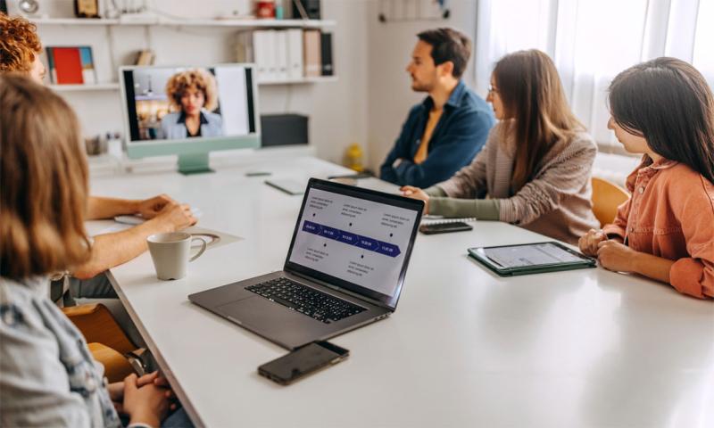 Board members around a table meeting with another board member remotely.