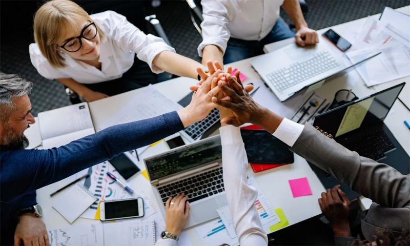 Co-workers putting their hands together in a huddle around an office table.