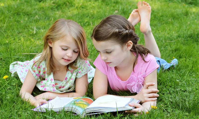 Two children reading a book on their lawn.