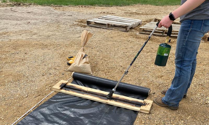 Gardener using a torch to cut a strip of landscape fabric.