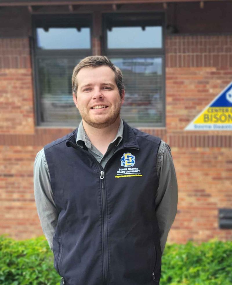 Logan Vandermark stands outside in front of a brick building