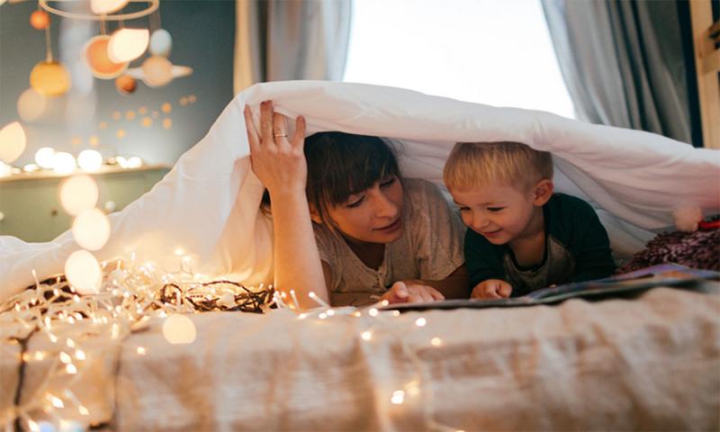 Mother and son reading bedtime story under a blanket.