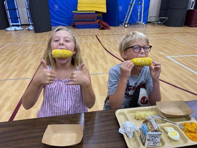 Two youth biting into an ear of corn