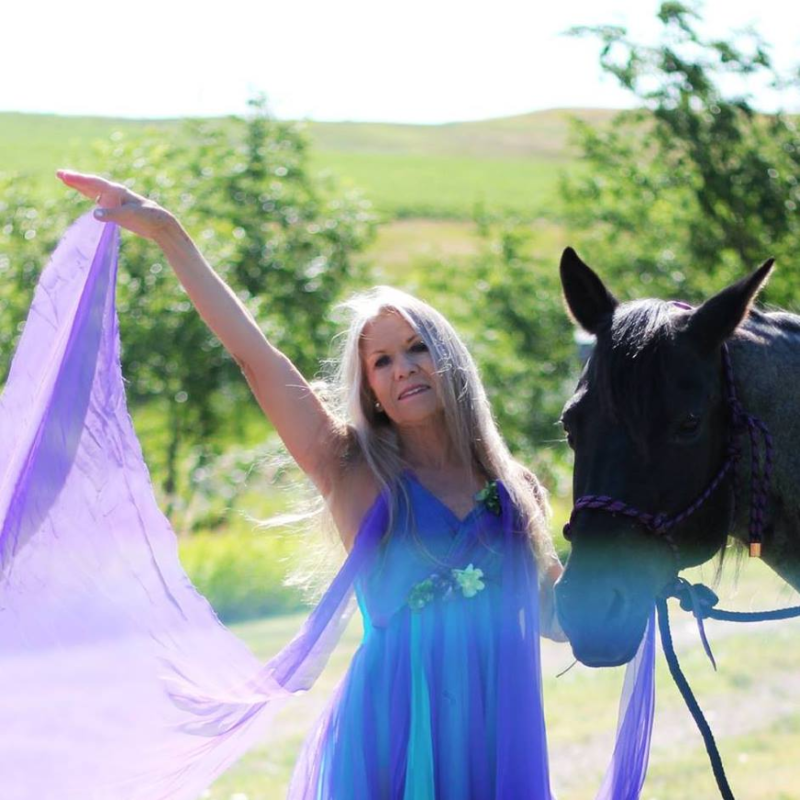 Sunny Hannum, a dancer based in Fort Pierre, SD, dynamically posing with a horse in a field.
