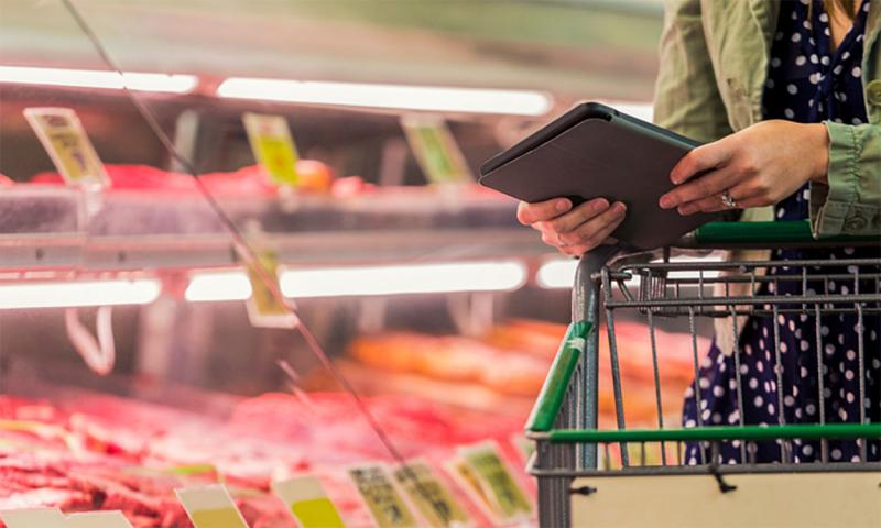 Woman with tablet examining ground beef at a grocery store.