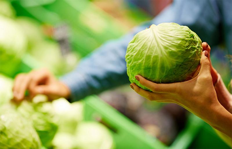 Couple choosing cabbage at a grocery store.