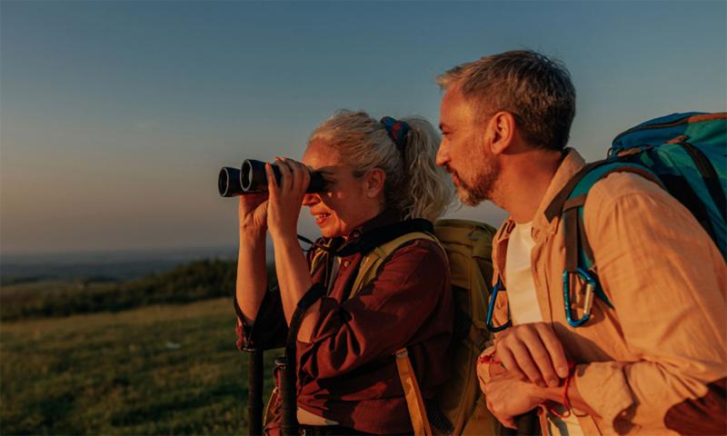 Middle-age couple uses binoculars during a sunset hike.