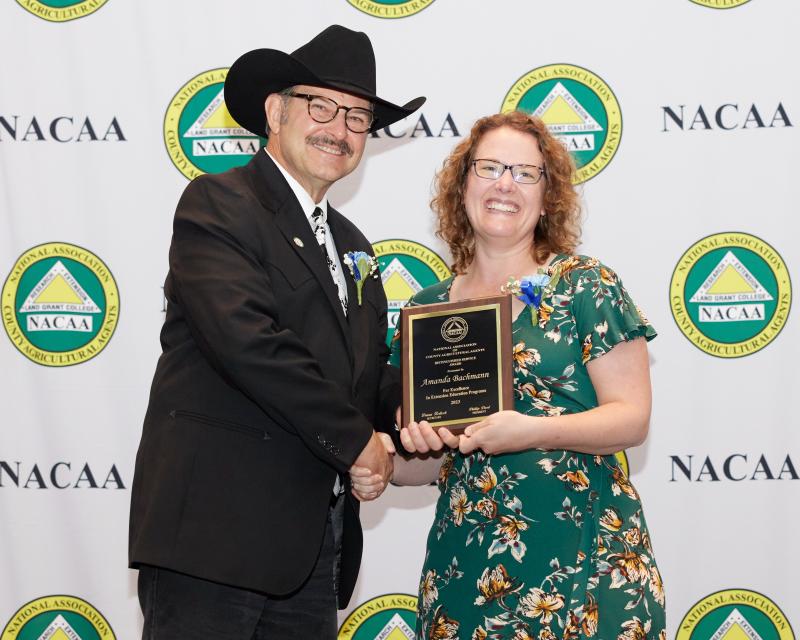 a man in a black cowboy hat hands a plaque to a woman with curly brown hair