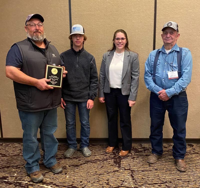 three men and a woman stand in a line smiling at the camera. the man at the far left holds a plaque for the Master Lamb Producers 2023 award
