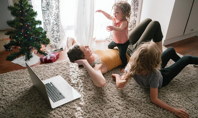 Mother and two daughters doing an online family fitness routine near a small Christmas tree.