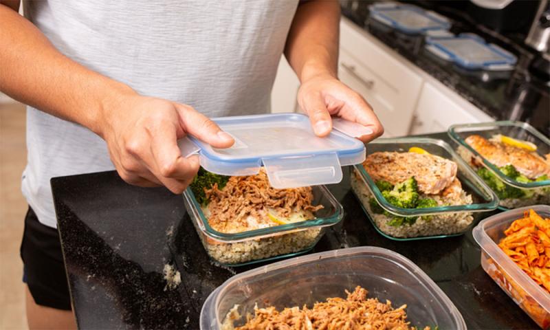 Man preparing several batches of pre-cooked meals for the week in plastic containers.