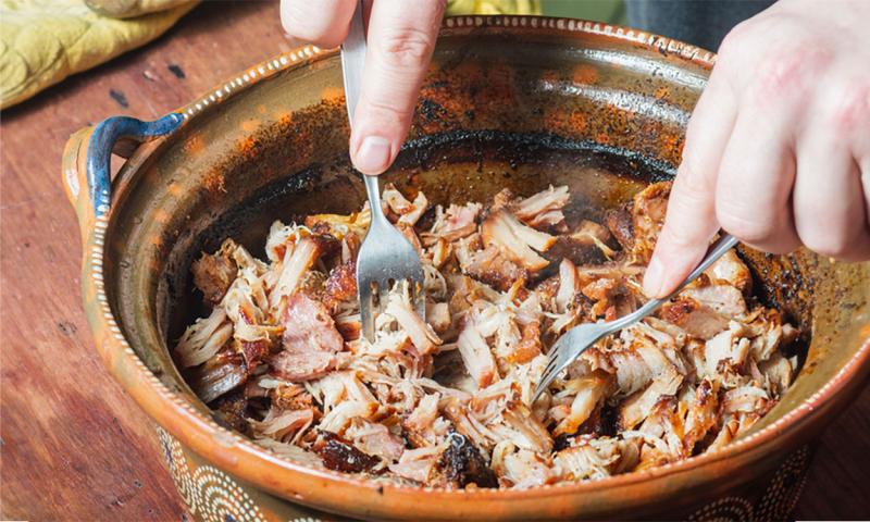 Pair of hands shredding a large batch of pork using two forks.