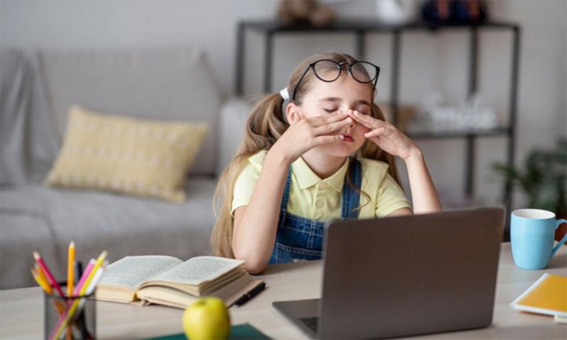 A tired young girl sitting at a laptop computer before school.