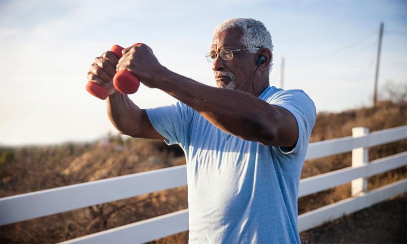 An older adult man exercising outdoors with dumbells.