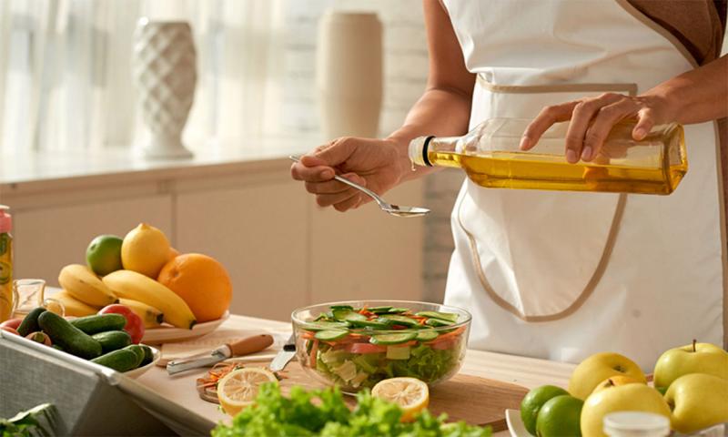 Chef pouring olive oil over a vegetable salad.
