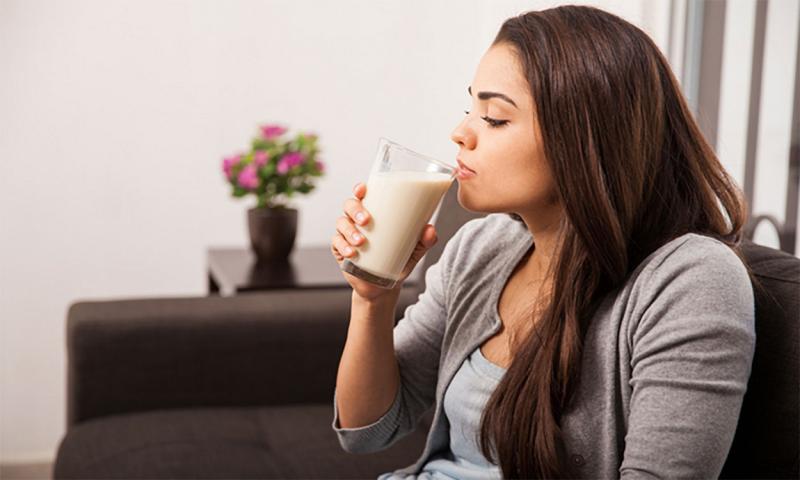 Young woman taking a small sip of milk from a glass.