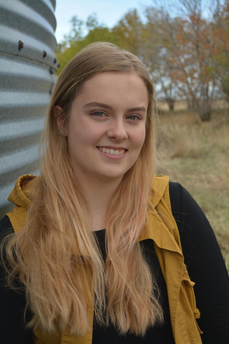 Bobbi Eide smiles at the camera. She's standing outside in front of a metal grain bin