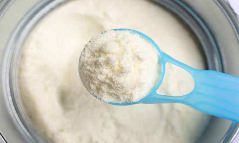 Plastic scoop over a container of powdered infant formula.
