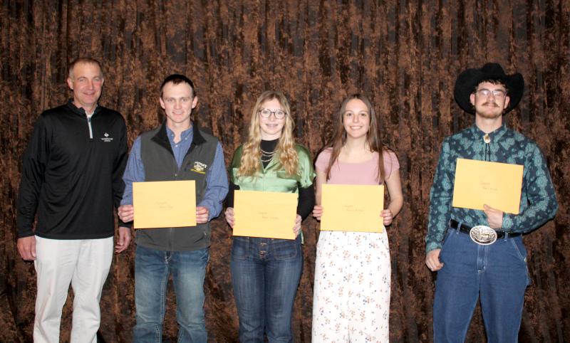 four students smile at the camera holding large manila envelopes next to the man who presented them with the scholarships