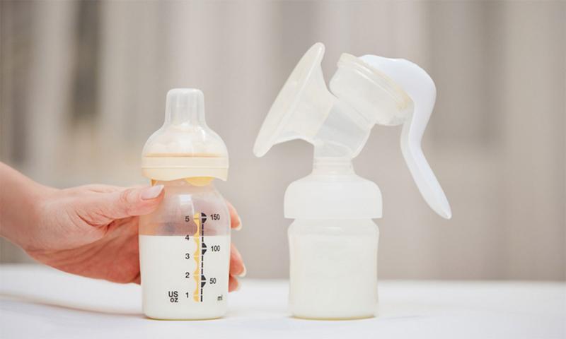 Hand reaching for a bottle of breastmilk near a manual breast pump.