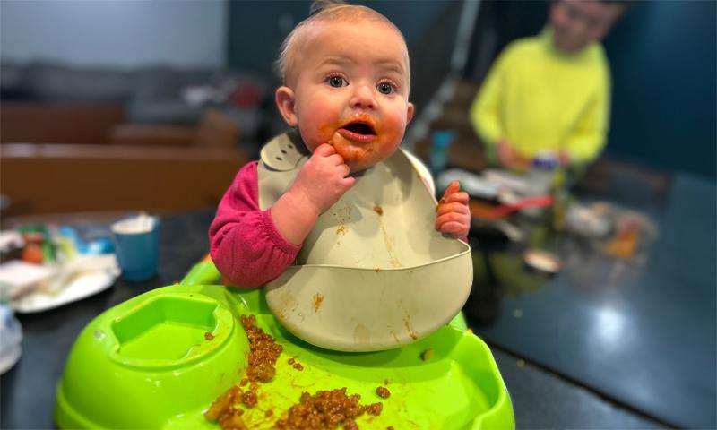 Infant with a bib trying small pieces of chili in a training seat.