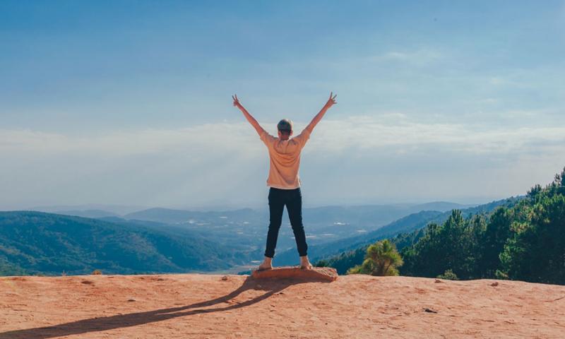 Young woman holding her arms in the air while overlooking a mountain range.