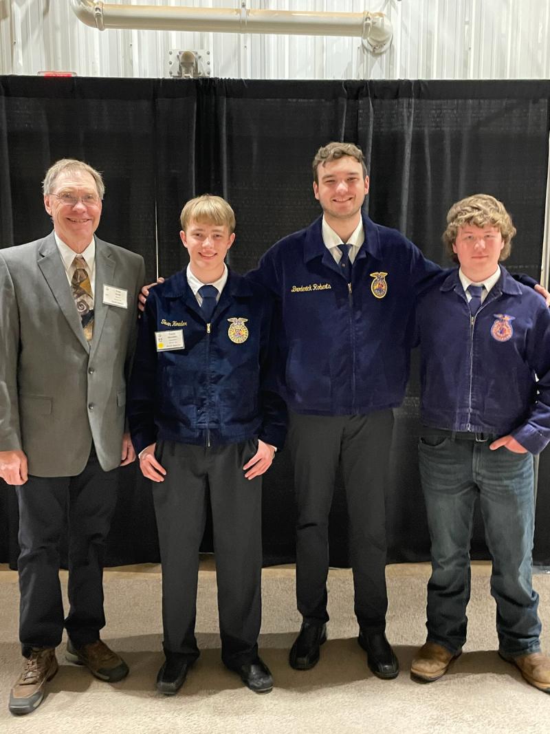 Three people in matching FFA shirts smile at the camera. Their coach is on the left in a grey suit jacket