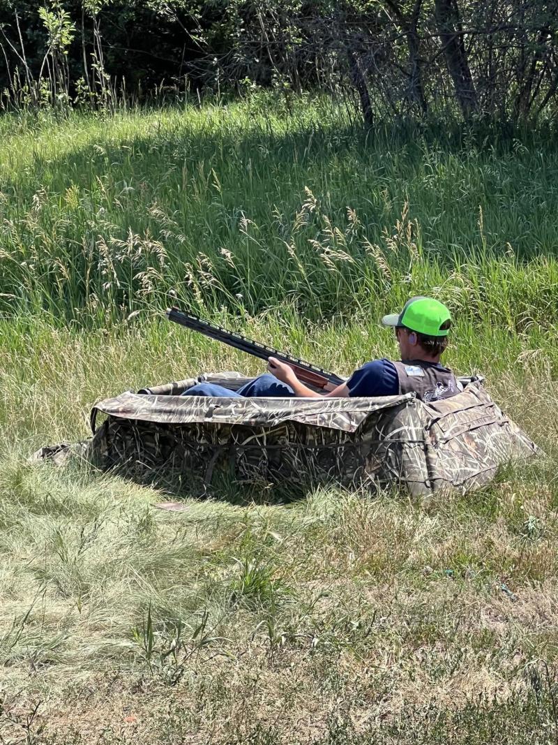 A youth sits in a hunting blind holding a shotgun