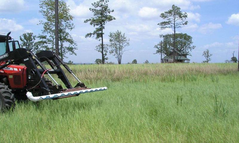 Tractor-mounted wick applicator applying herbicide to a pasture.