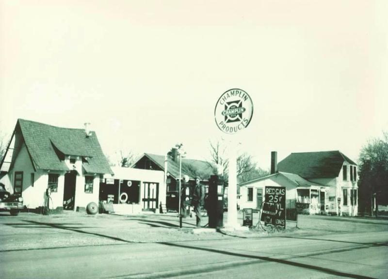 a black and white photo of the Lake Preston gas station with the McCrory Garden cottage on the left side. a parking lot with a gas pump is to the right