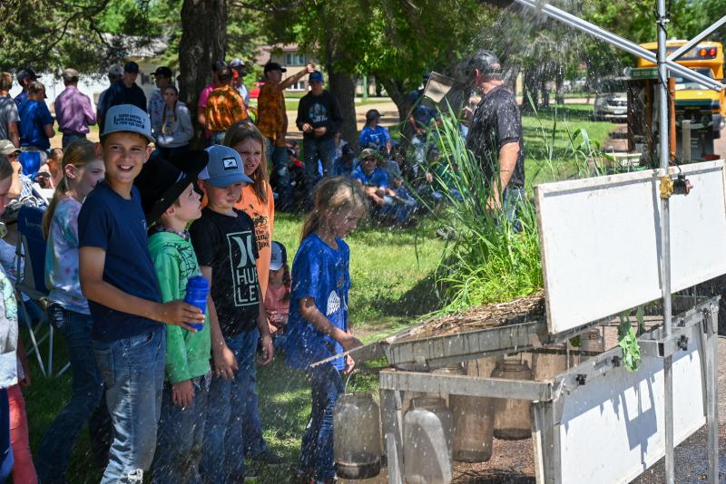 A group of children stands in front of a display with plants and simulated rainfall